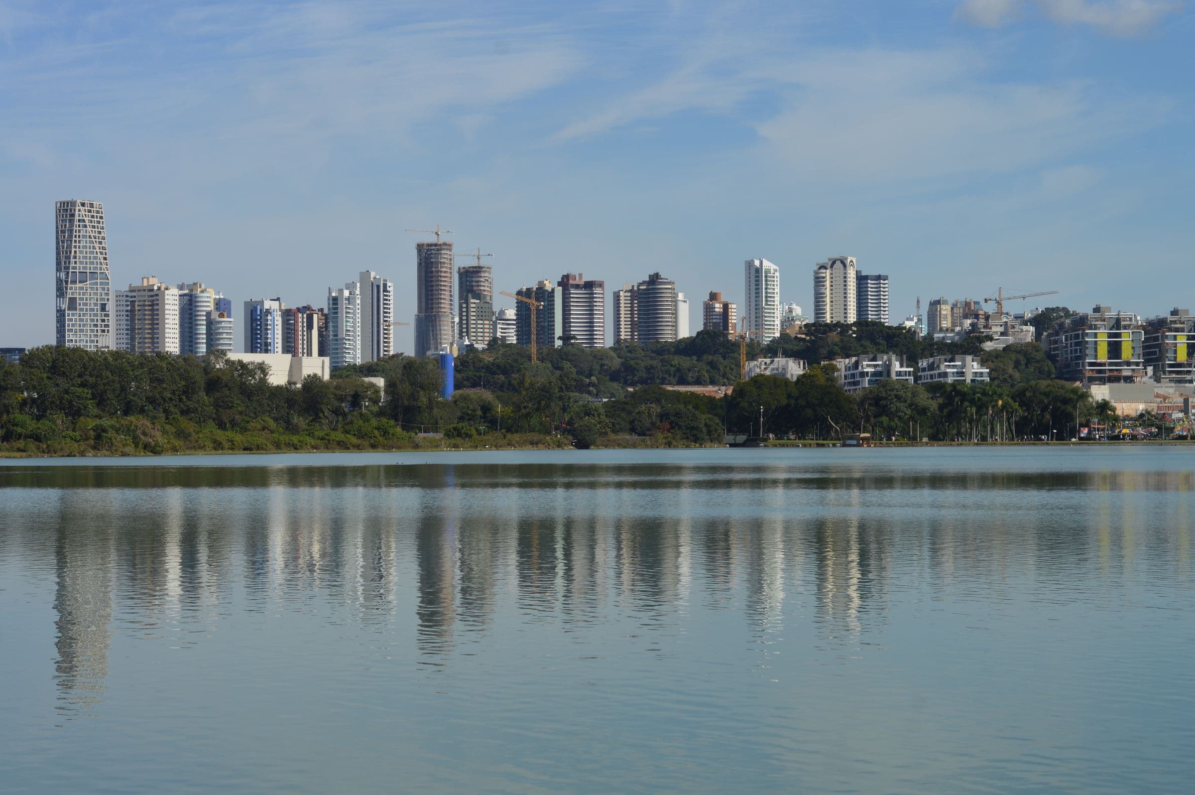 Skyline de Curitiba refletido no Lago do Parque Barigui, sob céu azul